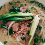 Bowl of chicken noodles soup with chunks of chicken, vegetables, and egg noodles, garnished with parsley on a wooden table